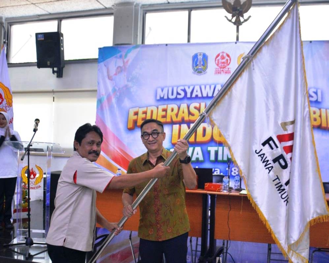 Momen sakral penyerahan pataka! Ketua Umum FPTI Jatim periode 2026-2030 terpilih, Henky Irawan (kanan), secara resmi menerima bendera kebesaran dari mantan Ketua Umum Dhanu Iswara (kiri) dalam Musprov FPTI Jatim di Surabaya, Sabtu (18/4/2026). (jatimsport